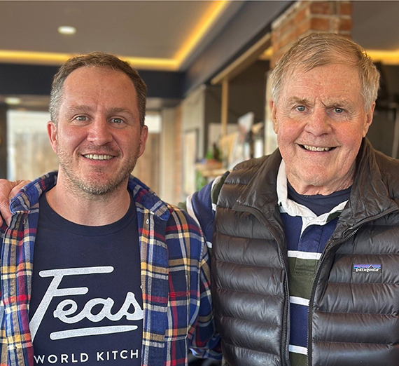 A group of five people stand together in a brightly lit hospital hallway, smiling at the camera. Two wear stethoscopes and medical attire, one wears a Gonzaga University sweatshirt, and others are dressed in casual or professional clothing, representing a mix of students and healthcare professionals.